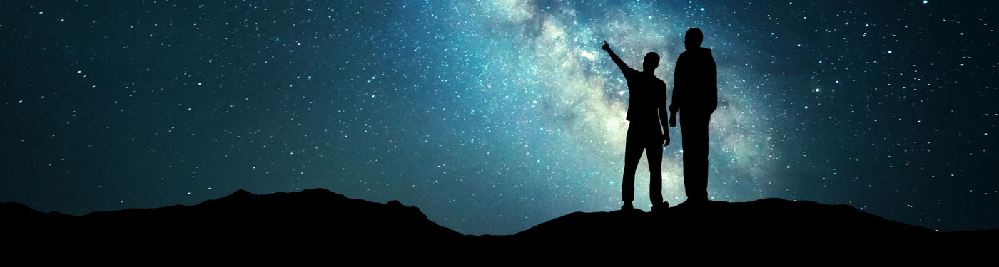 Silhouette of people pointing into a vast starfield